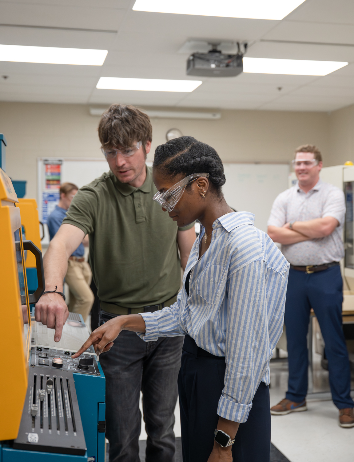 Two people wearing safety goggles interact with the controls on an injection molder in a Pennsylvania College of Technology polymers lab.
