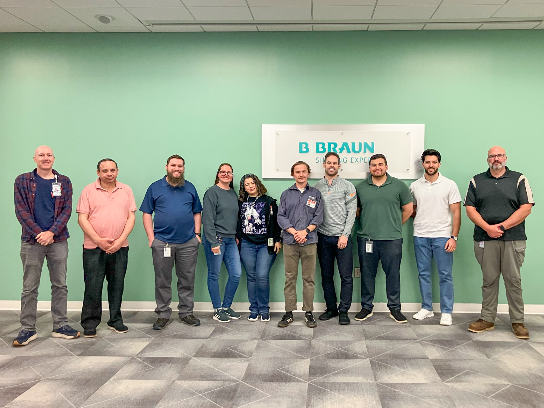 A group of 10 people stands in front of a green wall that has a B. Braun sign hanging on it.