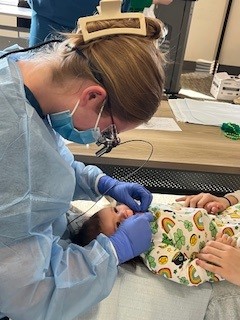 A student in protective medical gear examines an infant's mouth.