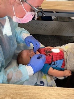 A student in protective medical gear examines an infant's mouth.