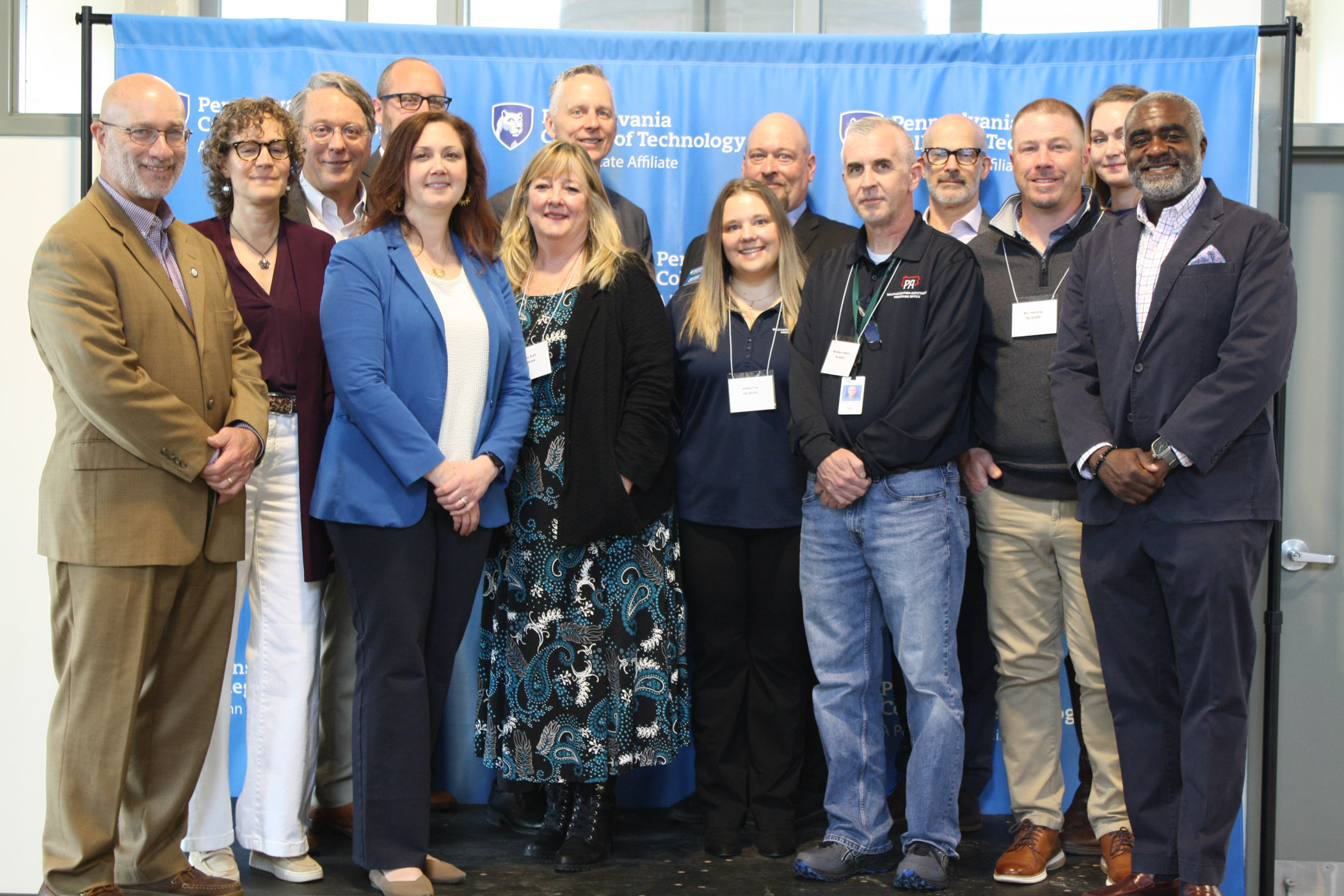 A group of 14 people gathers in front of a blue Pennsylvania College of Technology step-and-repeat banner.