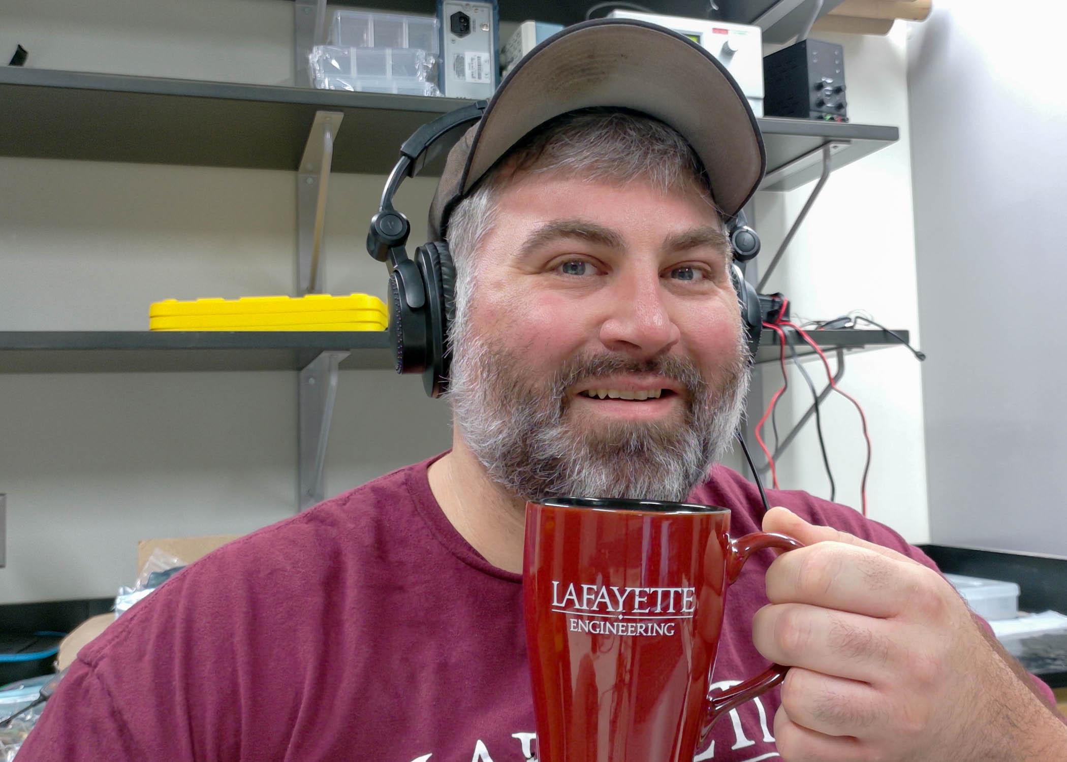 Robert Layng wears headphones over a baseball cap and holds up a coffee cup.