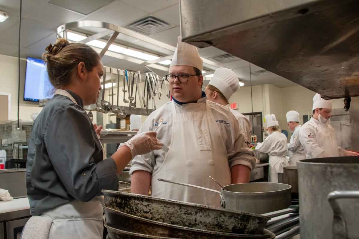 With a tasting spoon in-hand, Wisneski provides feedback to Caleb M. Taughinbaugh, a culinary arts technology student from Dover.