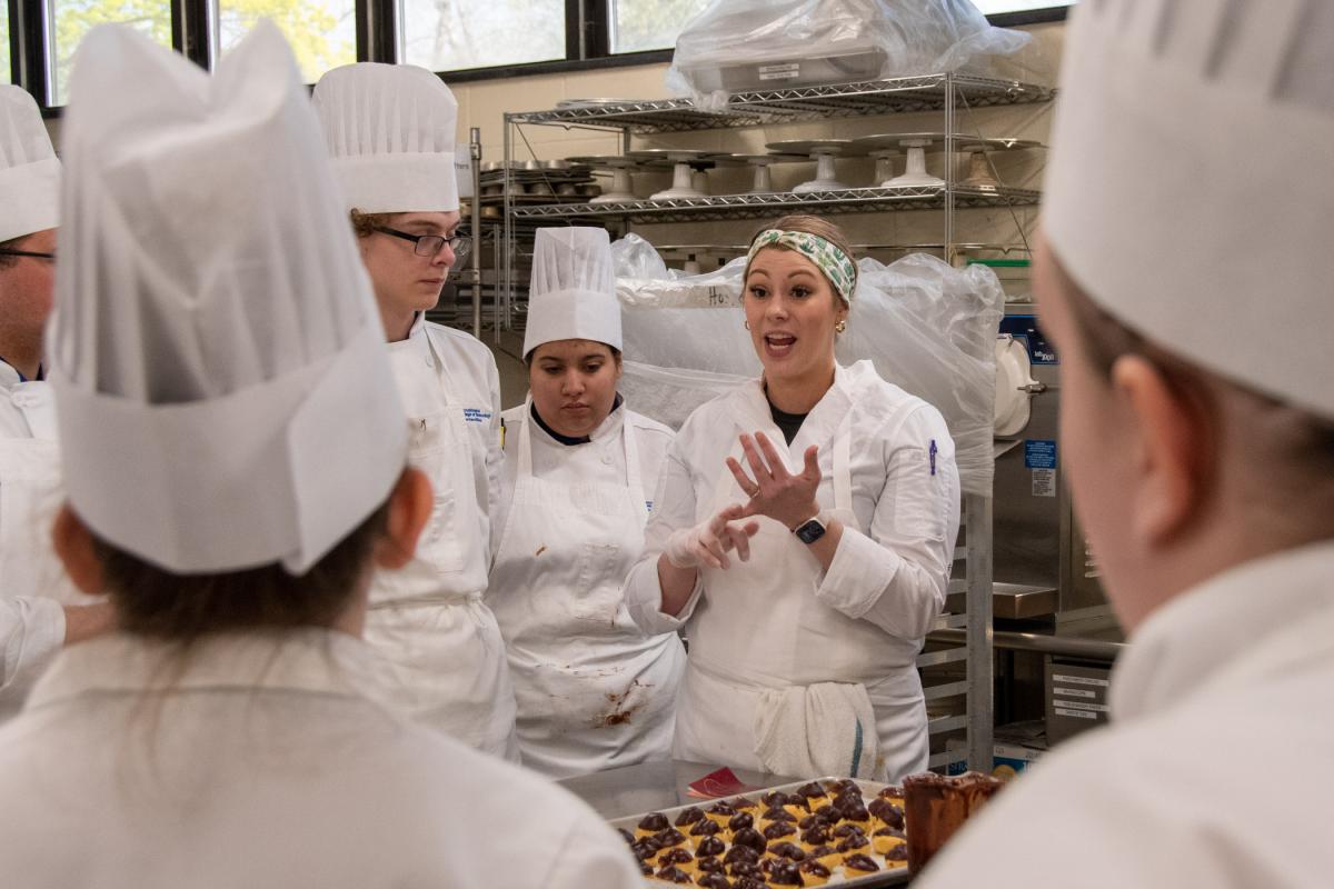 Summa talks with students about the final step in producing eclairs for the event – adding gold leaf.
