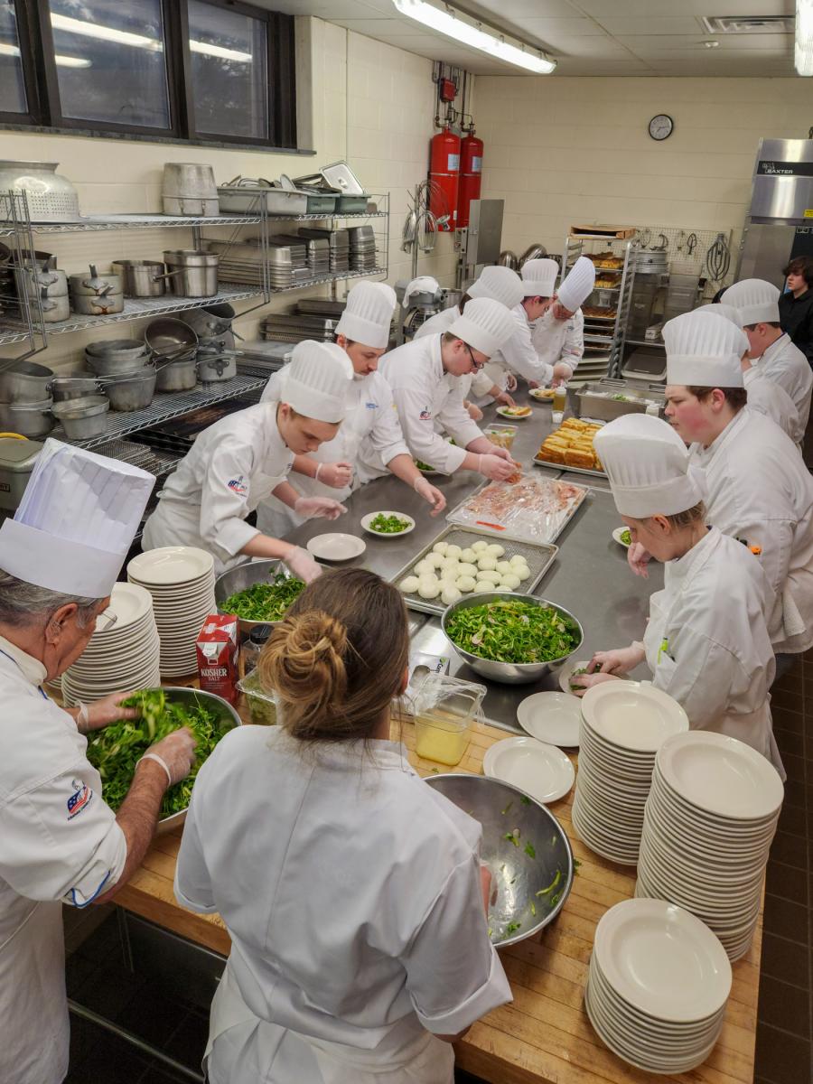 Students work, assembly-line style, to plate the first course: burrata salad. (Photo by Becky J. Shaner, senior manager of donor relations and special events)