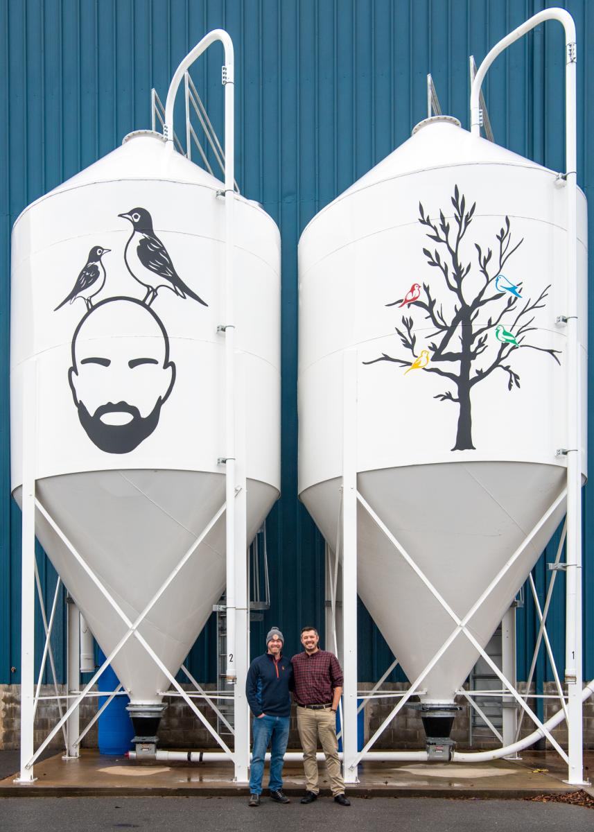 A research partnership takes flight. Feerrar and Ingram stand beside the brewery’s grain storage silos. 