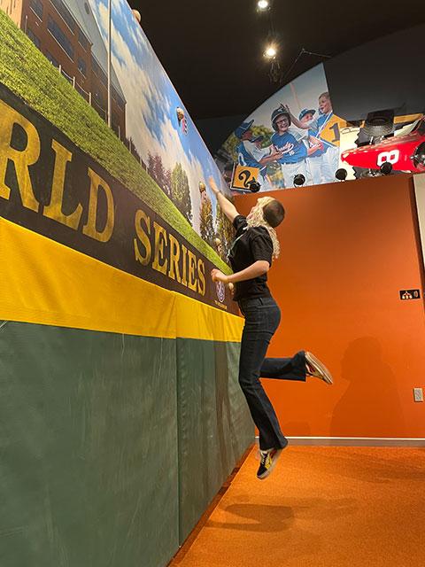 Blaithin Skeet goes airborne at the museum's jumping wall, leaping to snag a ball as it threatens to clear the outfield fence.