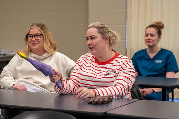Comically pointing a rubber chicken (used as a talking piece as the visitors shared their backgrounds) is NWRC’s Stephanie McGuinness. Bláthnaid Leonard (left) and Veronica Speer (back right), a Penn College dental hygiene student from West Falls, N.Y., listen in. 