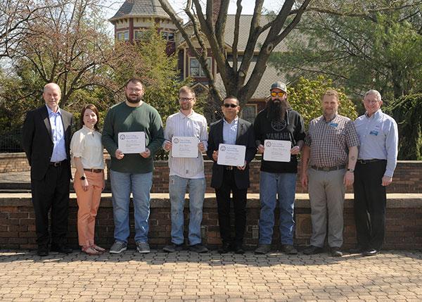 Four members of Pennsylvania College of Technology’s latest apprenticeship graduating class – part of a 12-member group that includes a number of out-of-state journeyworkers – gather with supporters near The Victorian House.