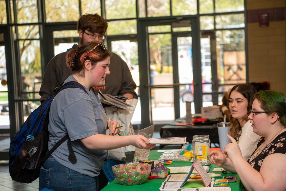 At one of six tables staffed by PSY335 students, graphic design student Emily M. Scaife hands in a worksheet she completed focused on avoiding end-of-semester burnout. (Focused on a holistic approach to clinical mental health, the class introduces students to the way clinical psychologists conceptualize, assess, diagnose, treat, and prevent mental and physical health issues.)