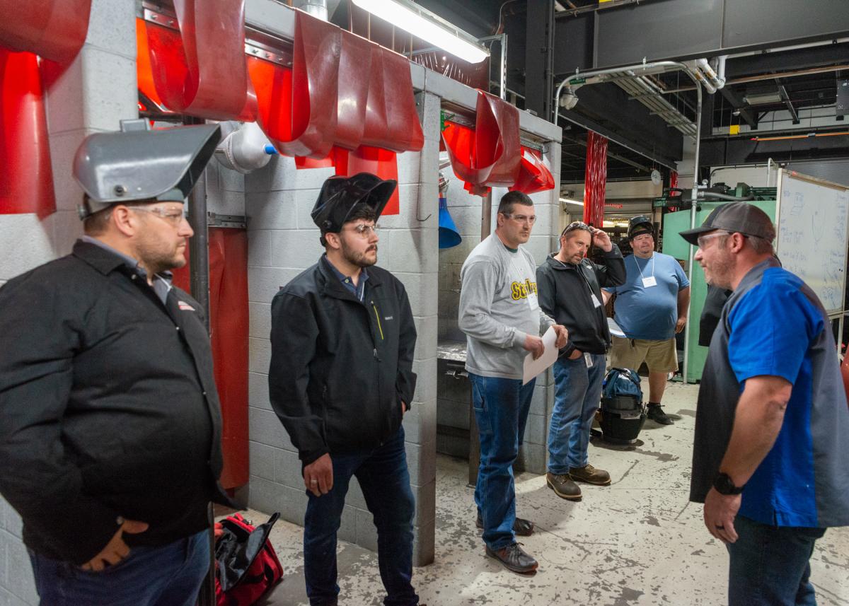 Ryan P. Good (right), assistant professor of welding, talks with welding educators outside a row of welding booths in the college’s 55,000-square-foot Lycoming Engines Metal Trades Center.