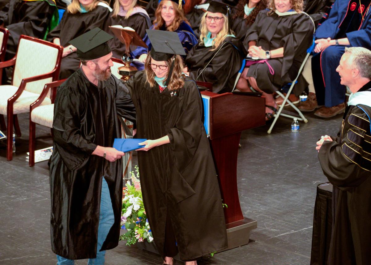 Among several college employees with family members in the graduating class, Katie L. Mackey, assistant director of disability and access resources, presents a diploma cover to husband, Jon W., who earned a bachelor's in emergency management & homeland security. 