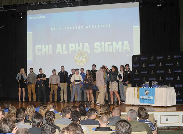 Chi Alpha Sigma inductees gather on stage, where Kelly B. Butzler, chemistry professor and Penn College's faculty athletics representative, presented them with their honor cords.