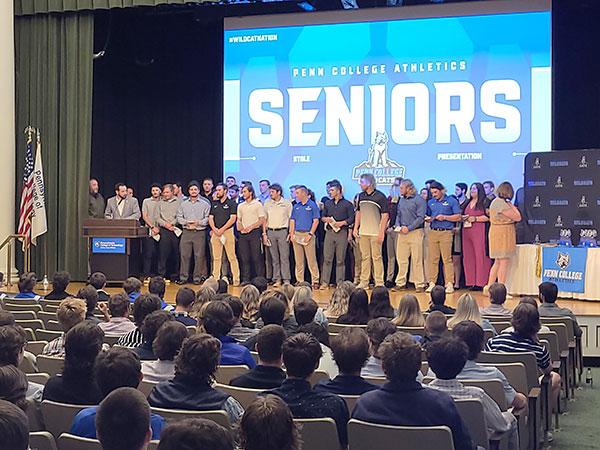 A scrum of seniors scrambles to the auditorium stage to receive graduation stoles from their respective coaches.