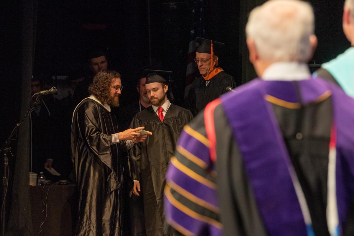 Anthony J. Pace (left), dean of enrollment and academic operations, was tasked with reading (and correctly pronouncing) each of hundreds of names – and, where applicable, any achievement awards won by the students who crossed the stage. 