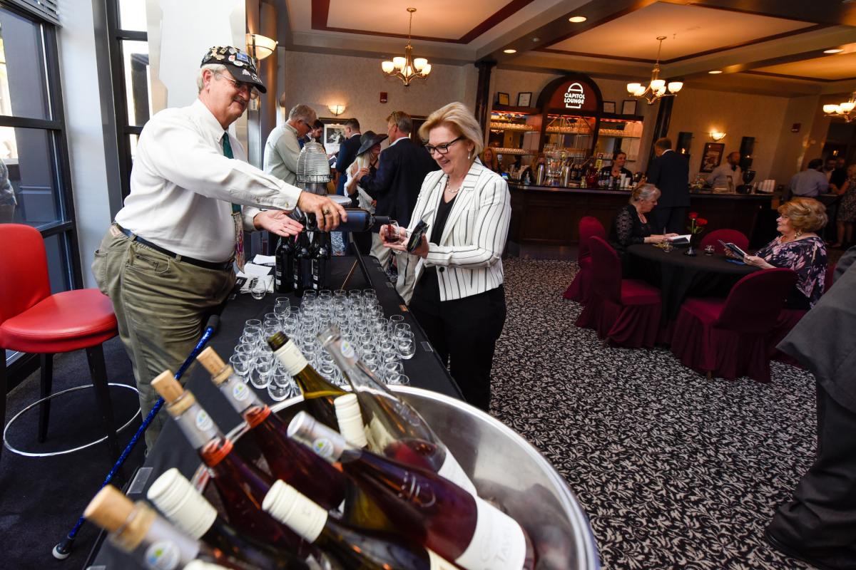 Showing off his sommelier's skill set, Chef Paul Mach, retired Penn College culinary faculty, pours a sample for Nesli Alp, vice president for academic affairs/provost.