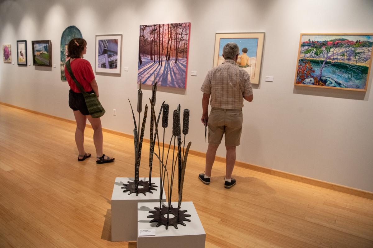 Gallery-goers take in an array of artwork, including (in foreground) “Summer & Winter Cattails,” metalwork by Anne Alexander. 