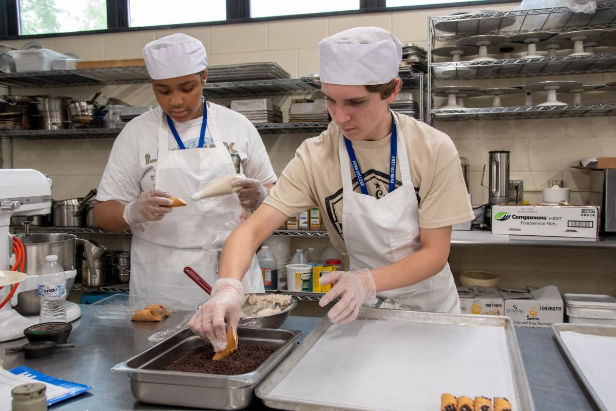 In the baking lab, future restaurateurs team up to fill cannoli with a cinnamon cream, then dip the ends in mini chocolate chips.