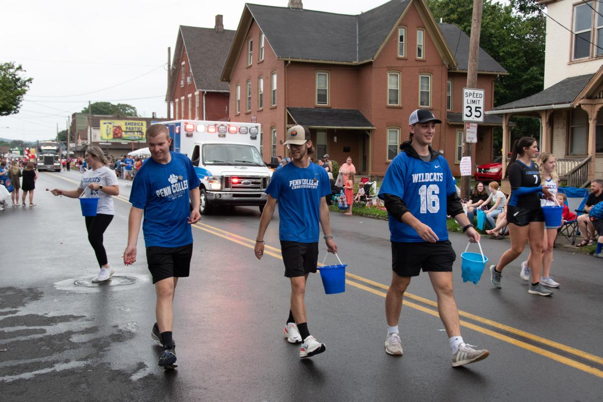 A group of student-athletes hands pins to viewers near the college’s Center for Business & Workforce Development.