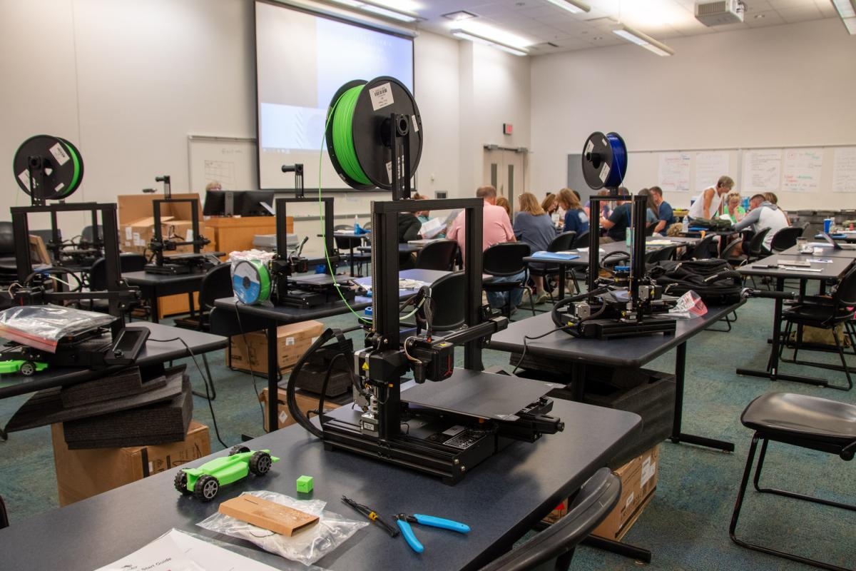While middle school educators collaborate on the other side of the room, 3D printers – assembled by the attendees and used to make race cars – await their next command. The educators took the printers back to their schools for use in the classroom.