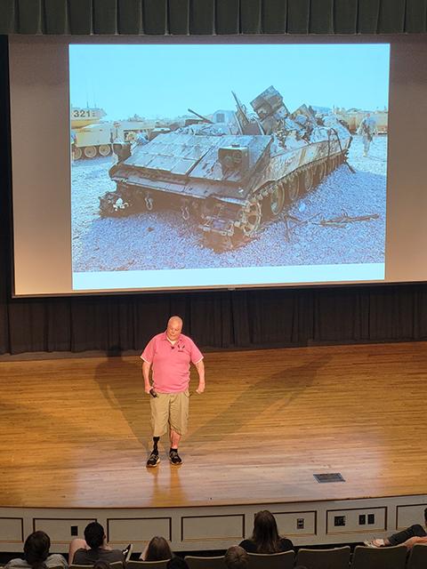 Retired Army Sgt. Rick Yarosh, standing before a 2006 photo of his burned-out Bradley fighting vehicle in Iraq, motivates participants to find the rewards on the other side of difficulty.