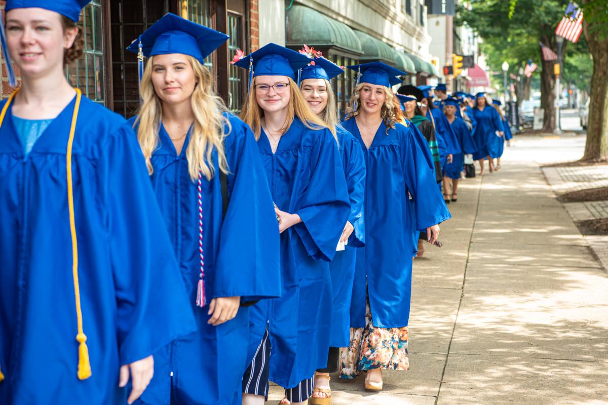 With flowers on caps and dresses, the graduates walk into the sunshine.