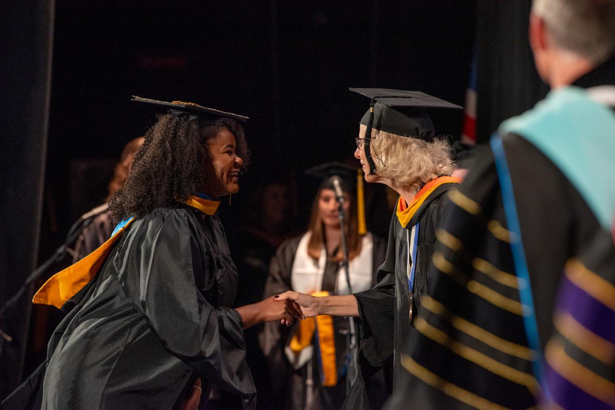 After receiving her hood, PA grad Kori-Ann Angelique Taylor turns to shake hands with Flynn.