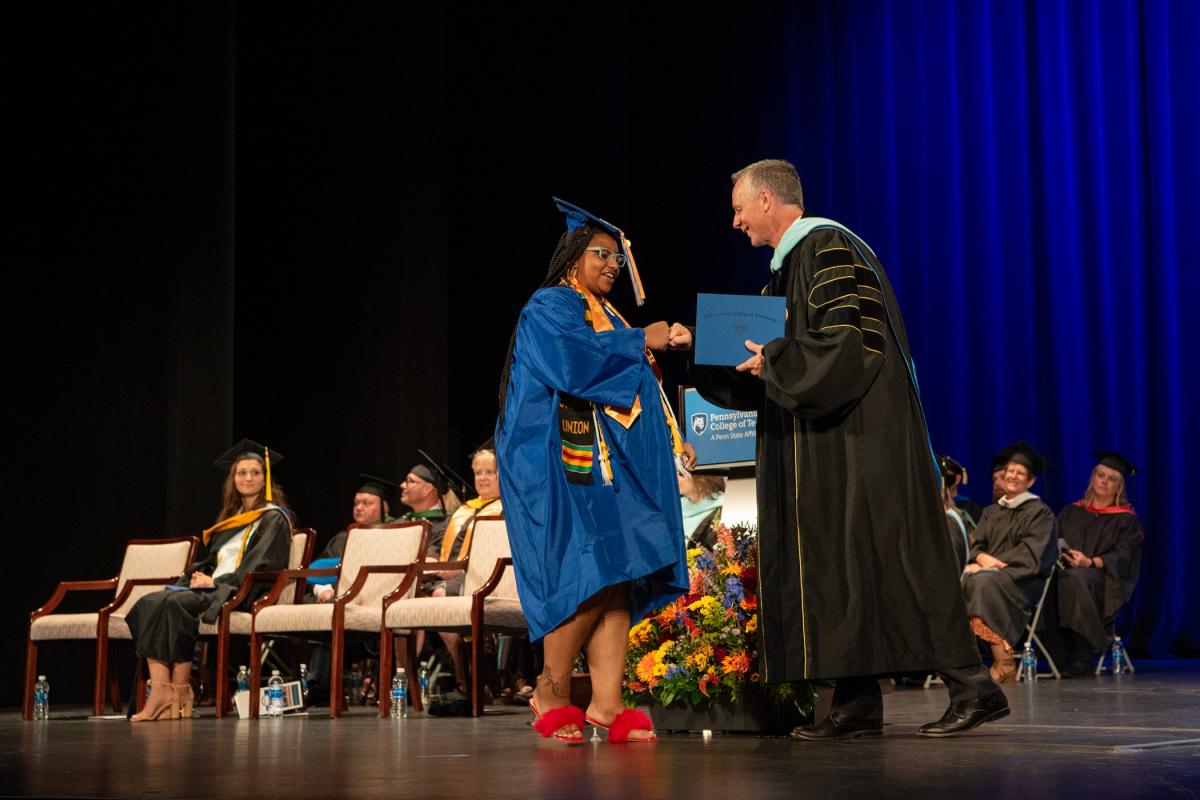 Human services & restorative justice graduate Monique C. Anderson-Parker enjoys a playful fist-bump with the president, who had asked students to signal how they wished to be greeted.