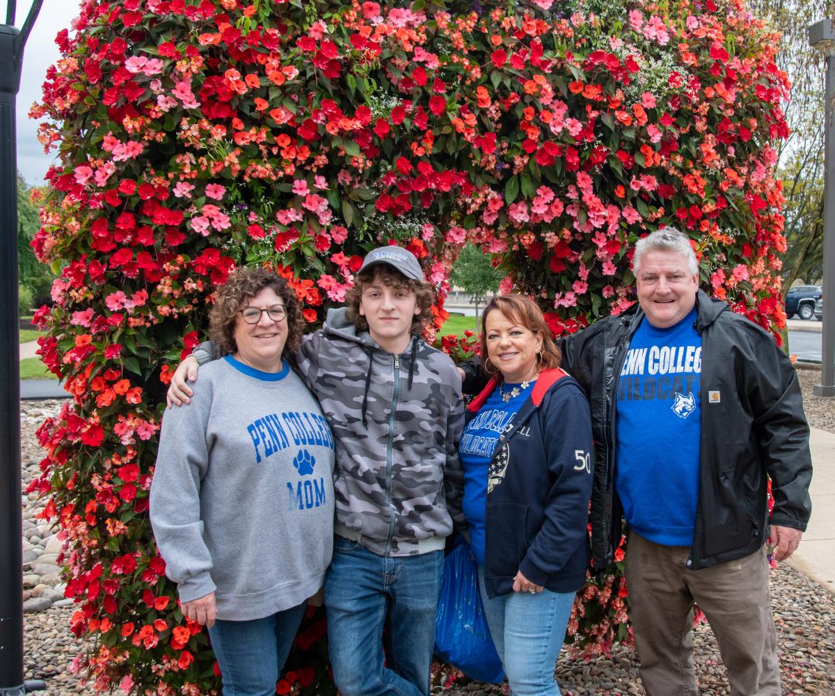 During a break in the rain, electrical construction student Tyler W. Eberle, with his mom, Wendy (left), aunt Leah and dad, Henry, grab a photo in front of a floral feature. Eberle is from Warren, N.J.