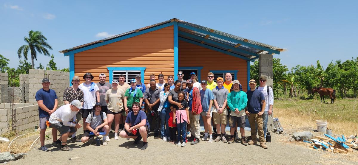Gathered around the six-member resident family that was with them all week, helping and offering food, the Penn College team celebrates completion of a home on its final workday in the Dominican Republic.