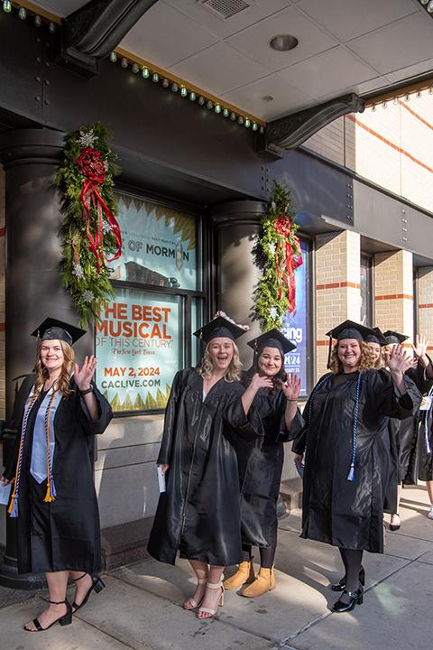 With holiday greenery behind them and a bright future ahead, a group of grads waves at a photographer.