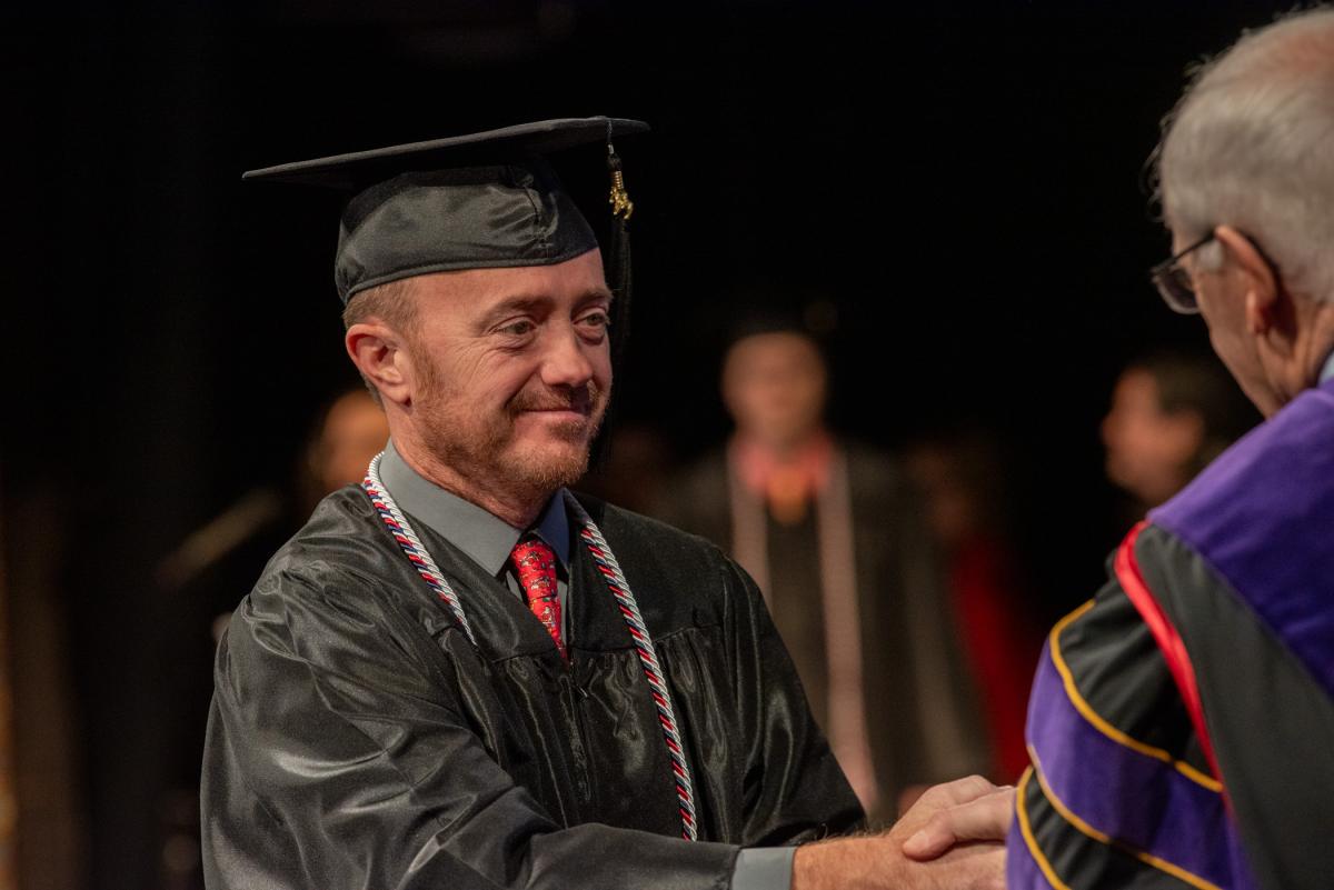 Veteran Jeremy N. Lakes, who earned a Bachelor of Science in business administration, shakes Yaw’s hand.