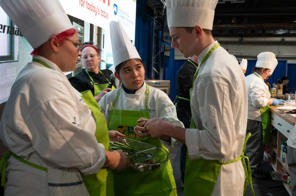 Students (from left) Ally A. Colon (baking & pastry arts), Alyssa D. Perez (baking & pastry arts), and Nicholas P. Matz (culinary arts technology) talk strategy during the School Cooking Challenge, which split Penn College’s cadre of Culinary Connection helpers into two teams to compete in front of the crowd as they each made an impromptu dish using surprise ingredients.