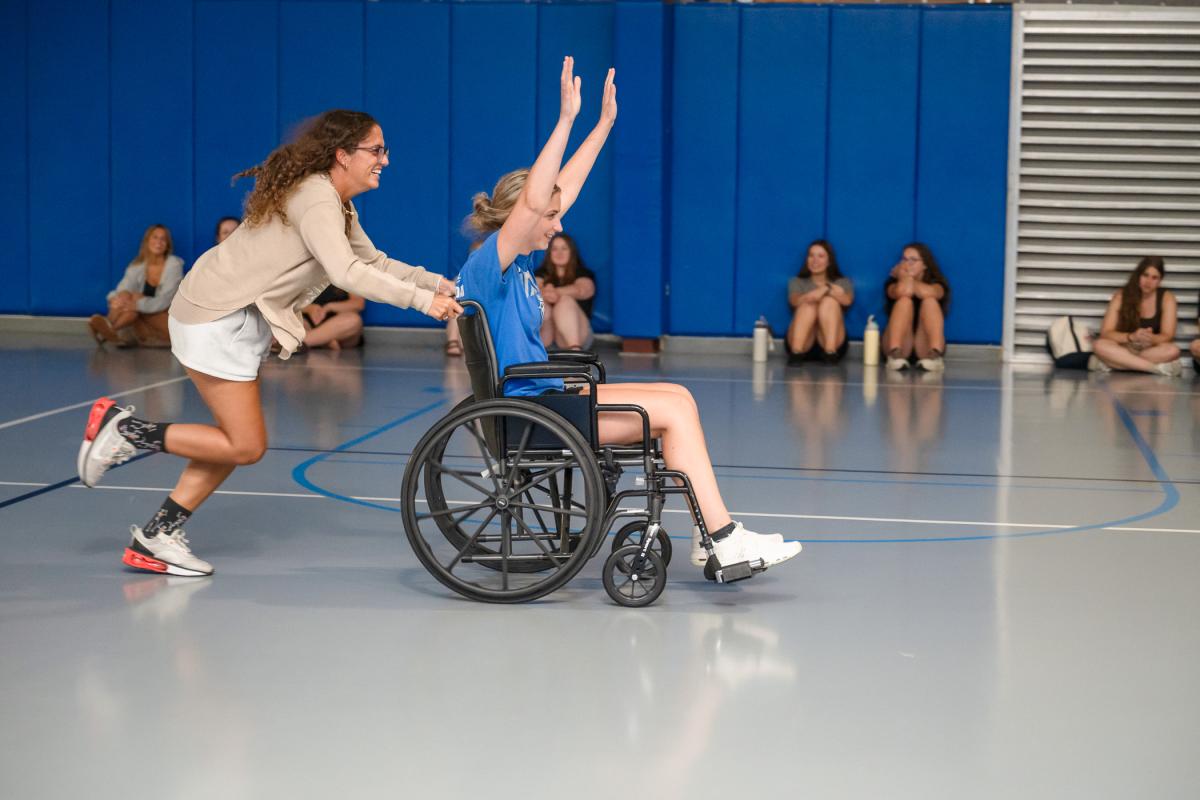 a student runs while pushing another student in a wheelchair