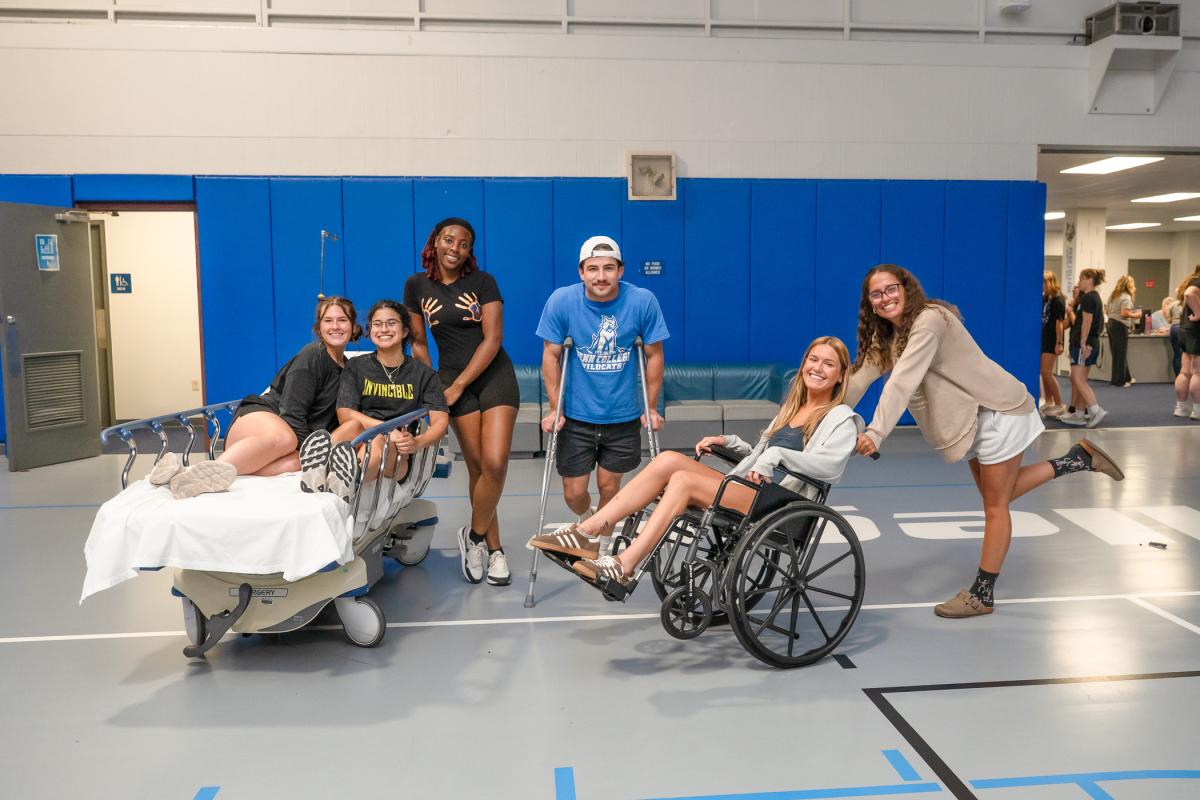 students pose with a hospital bed, crutches and a wheelchair