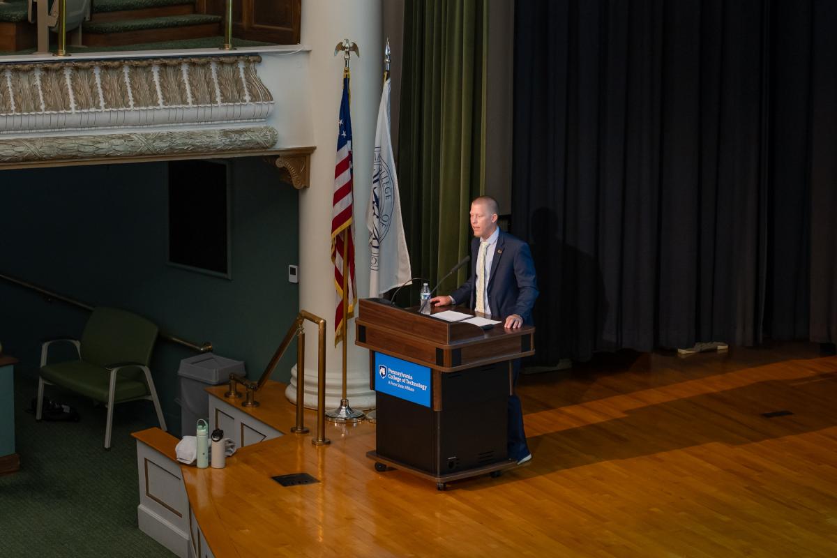 A man in a suit stands behind a lecturn on the stage of Pennsylvania College of Technology's Klump Academic Center Auditorium.