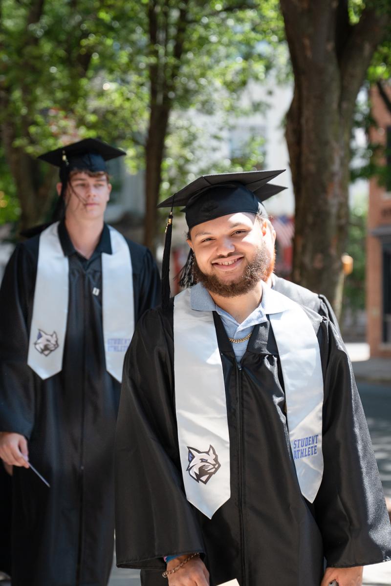 Students in caps and gowns walk toward the camera.