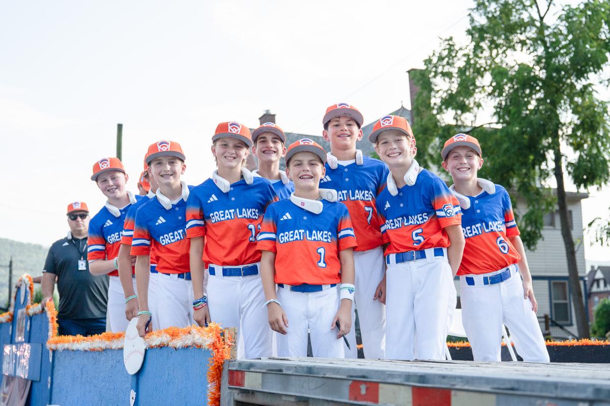 Boys in Great Lakes baseball uniforms stand on teh back of a decorated trailer.