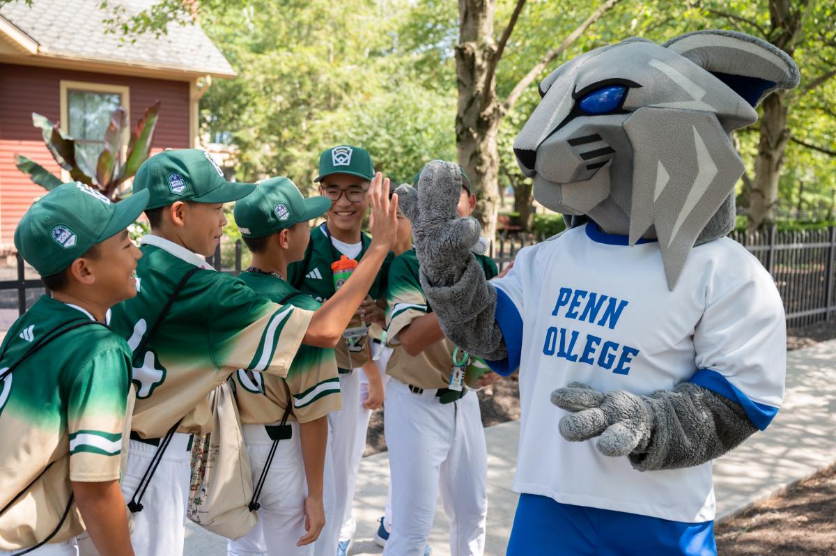Boys in baseball uniforms give high fives to the Penn College Wildcat mascot.