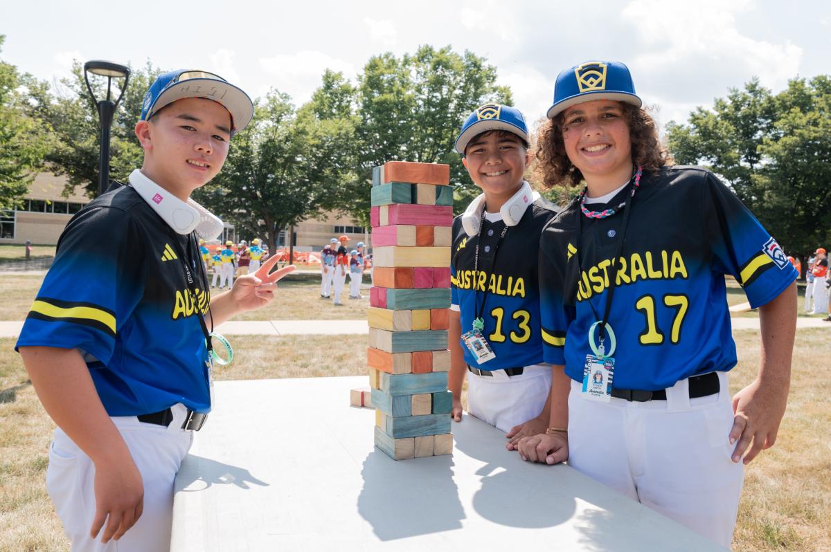 Boys in baseball uniforms stand next to a table with stacked blocks.