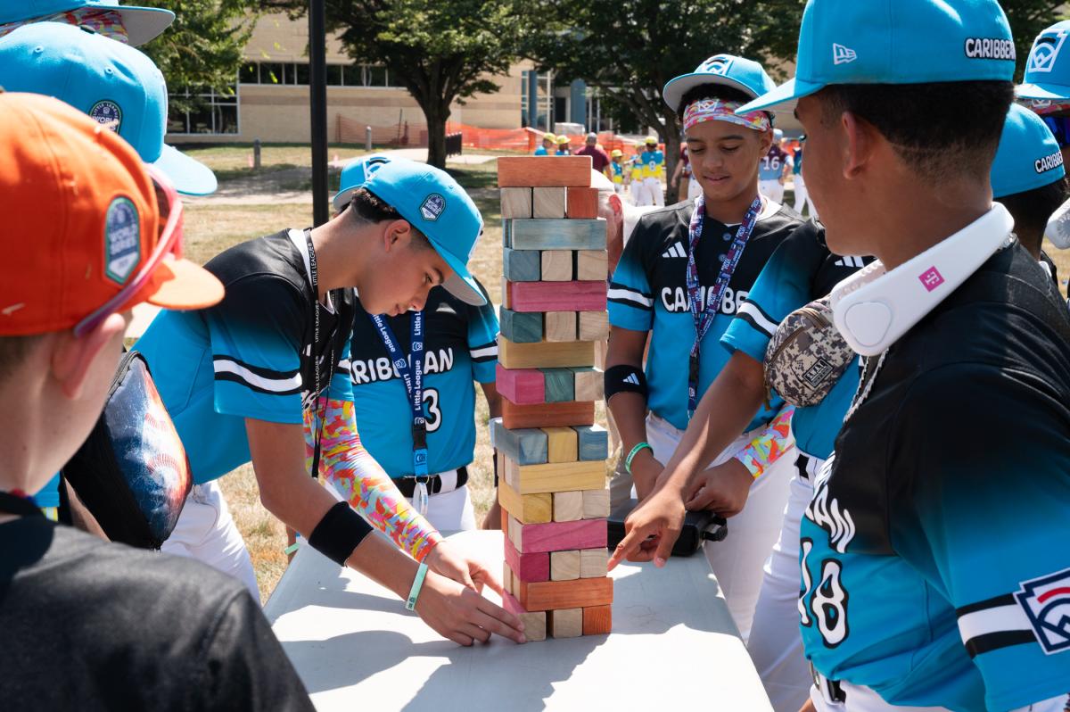 A boy in a baseball uniform tries to pull a block from the bottom a tower of wooden blocks.