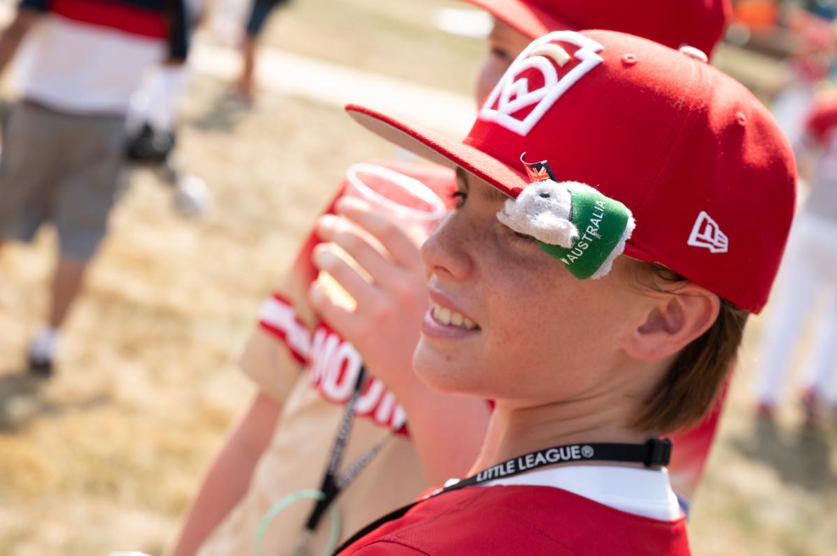 A boy in a baseball uniform, with a plush koala bear toy clipped to the brim of his baseball hat.