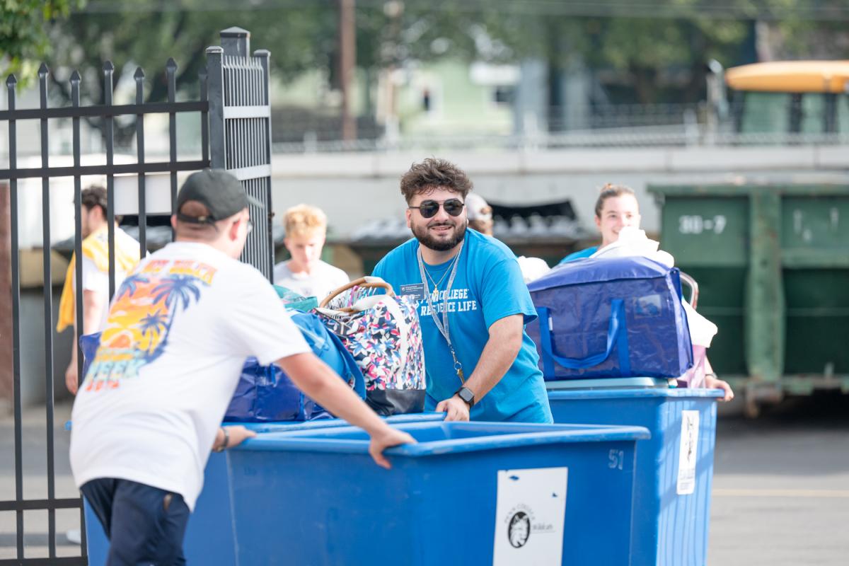 Students push large blue bins, some stacked with bags and other personal belongings.