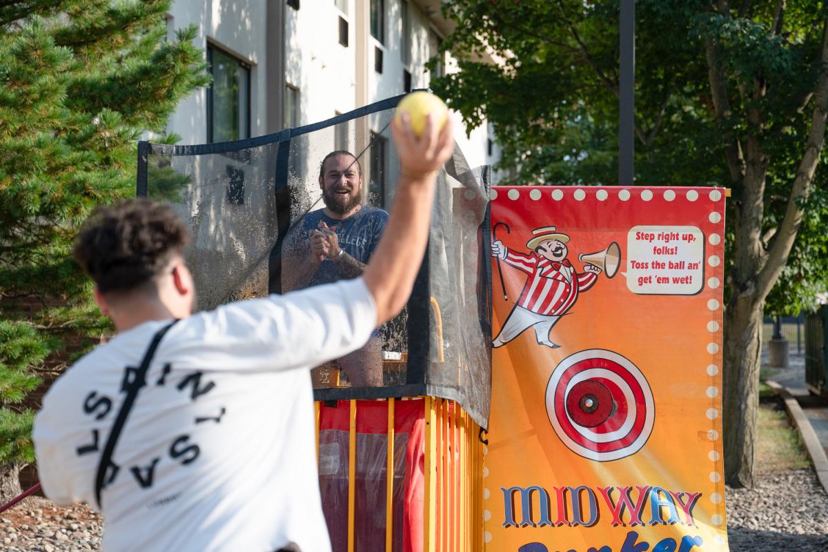 Pace sits in a dunk tank while a student prepares to through a ball at the target that will cause Pace to fall into the water.