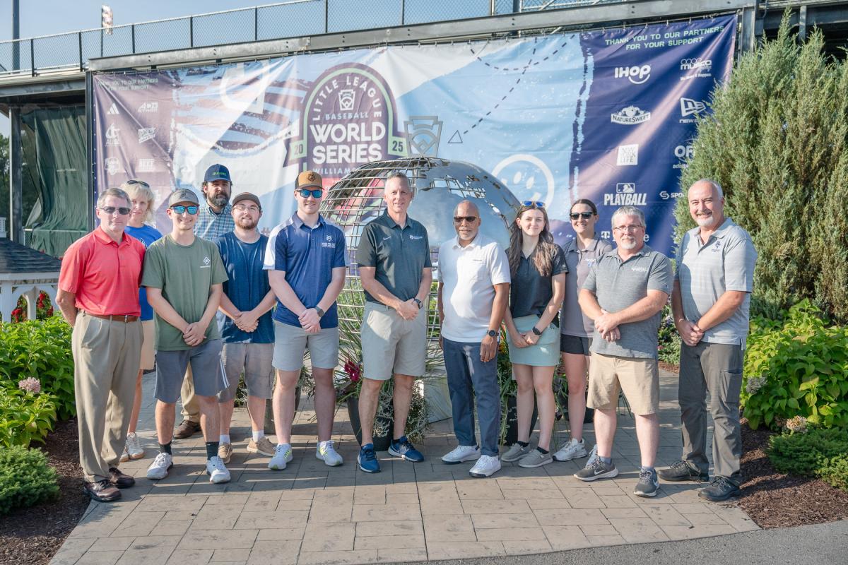 A large group stands around a stainless steel globe sculpture.