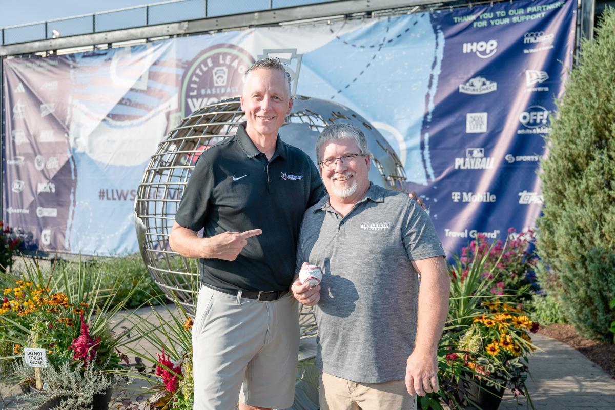 Michael J. Reed stands next to and points at Michael R. Allen, who holds a baseball. They stand in front of a metal globe sculpture.