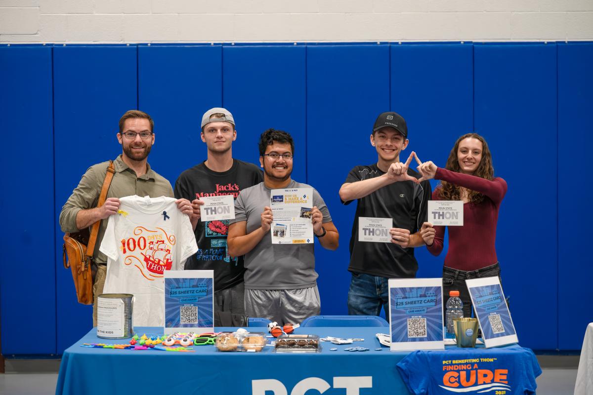 Students stand behind a table holding up posters, postcards and other THON-related information.