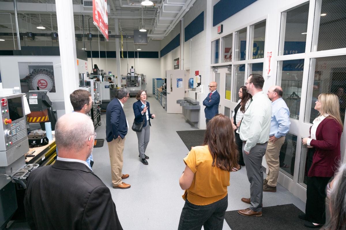 Inside a clean, bright space, people in business clothing gather near precision machining equipment.