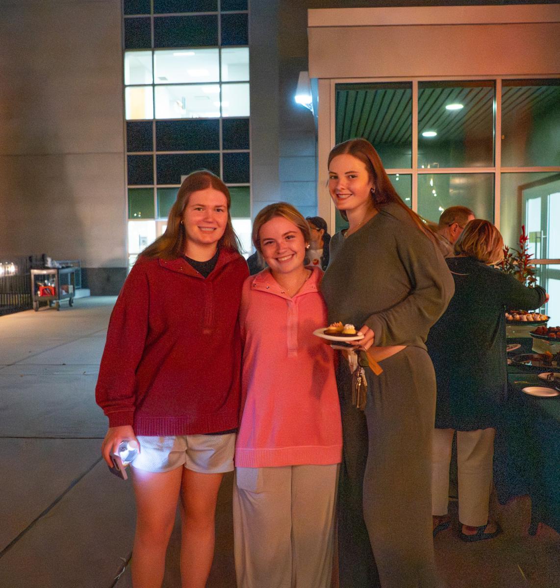Three young women pose, one holding a plate of desserts.