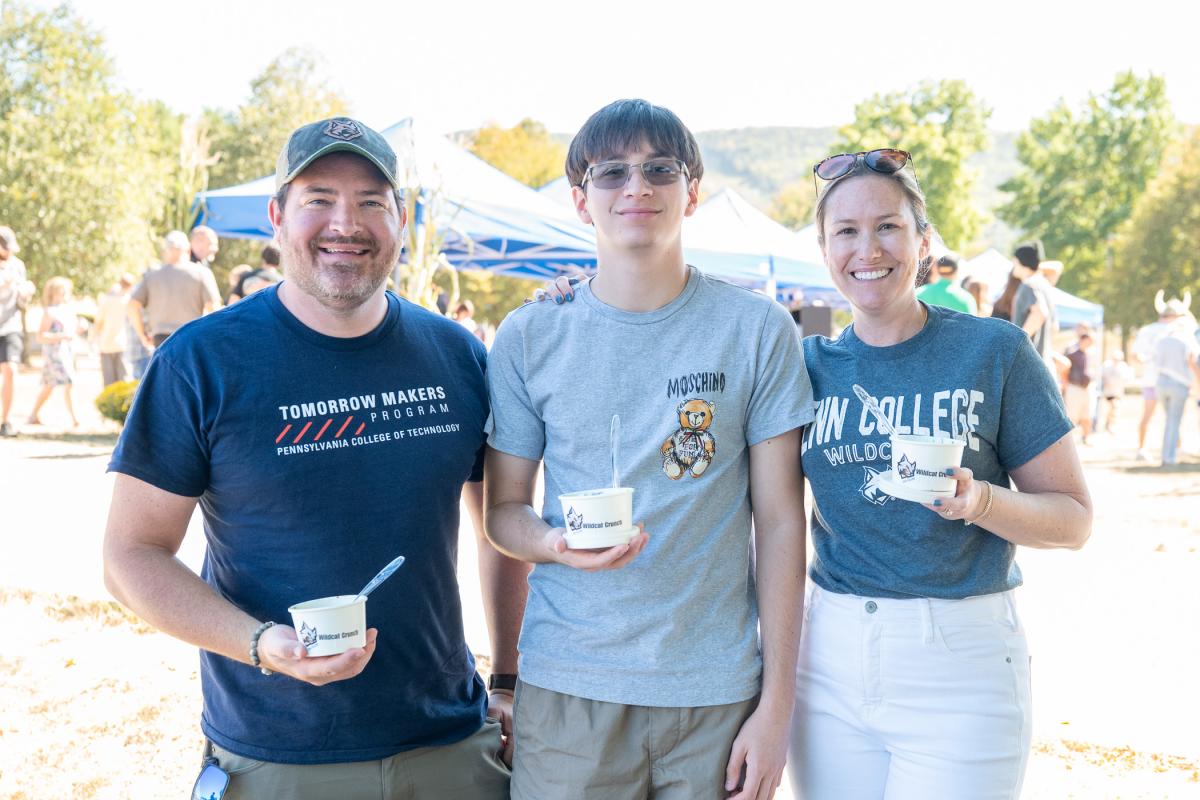A student stands between a man and a woman, all holding cups of Wildcat Crunch ice cream.